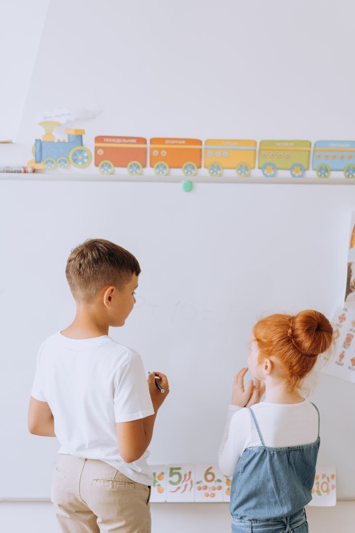 who-we-are Two young children engaging in learning activities at a whiteboard in a preschool classroom.
